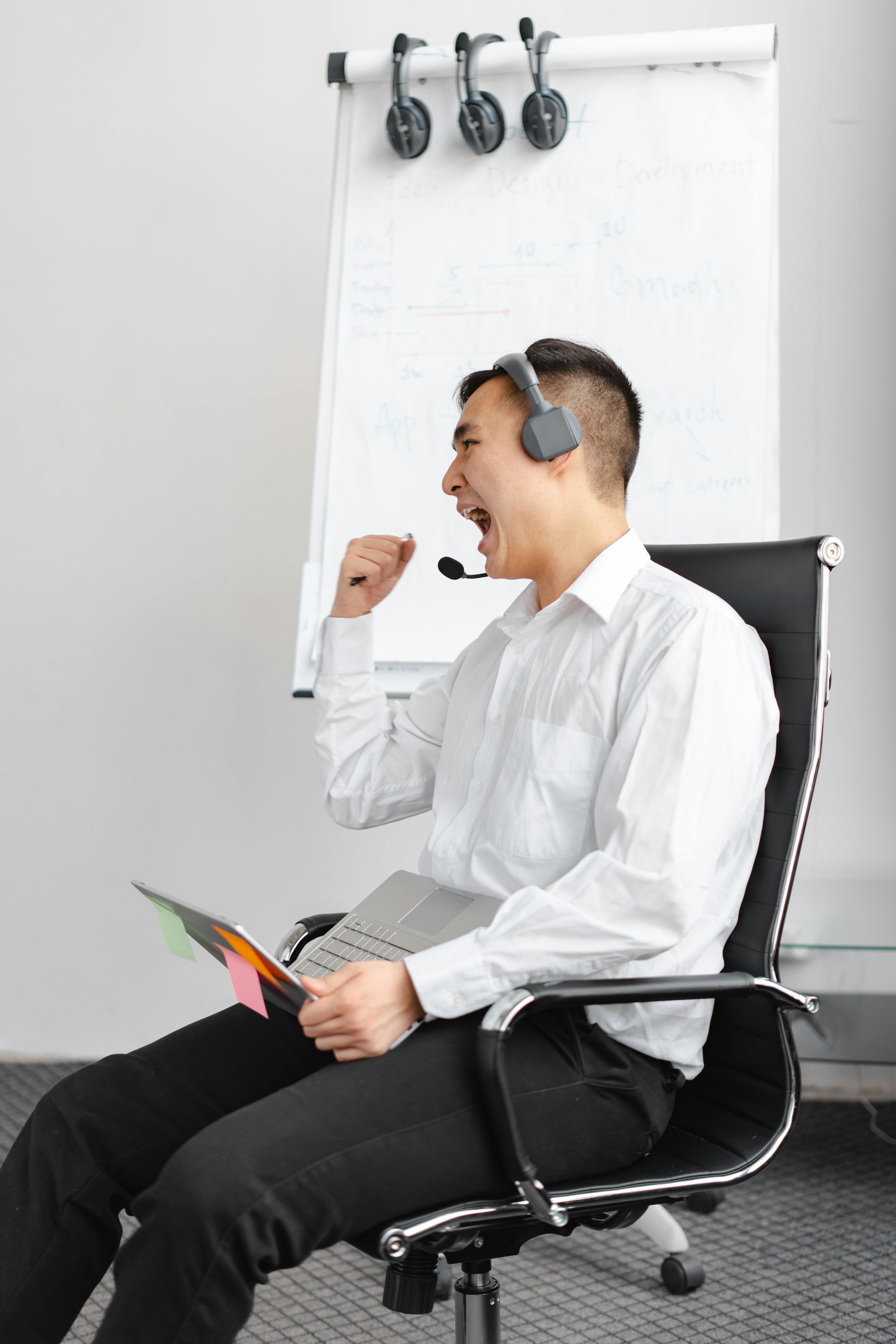 Excited call center agent with headset celebrates success while sitting in office chair.