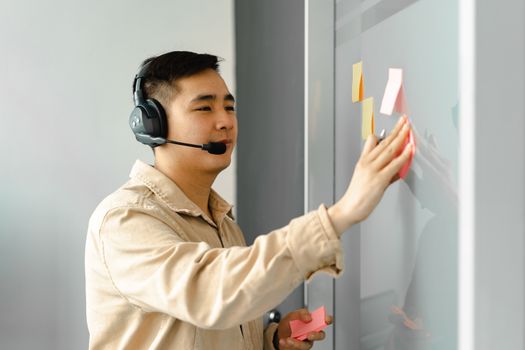 Business man using headset for a collaborative work session, placing sticky notes on a board.