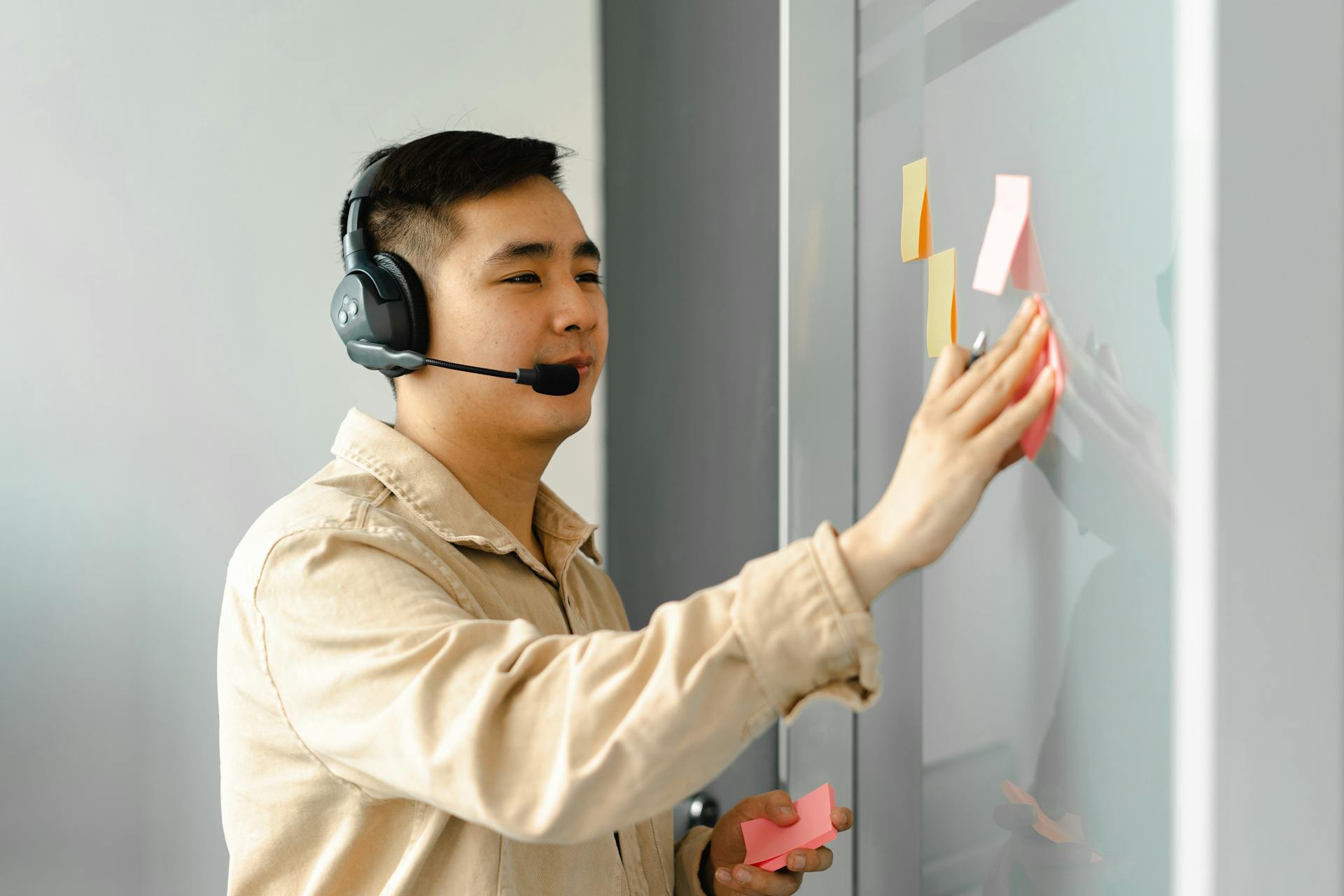 Business man using headset for a collaborative work session, placing sticky notes on a board.