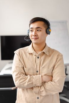 Confident Asian man at work wearing a headset, arms crossed, symbolizing modern communication.