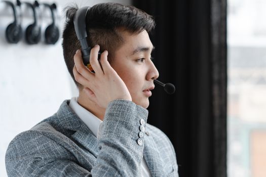 Side profile of a professional man wearing a gray suit and headset, communicating indoors.