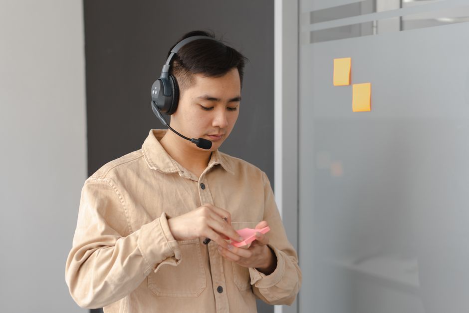 Jovem adulto em um ambiente de escritório usando fone de ouvido e notas adesivas. Ideal para visuais de comunicação empresarial.