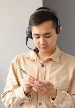 Asian male customer service agent wearing a headset, writing notes indoors.