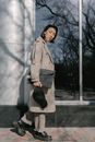 Woman in Gray Coat Standing Beside White Wall