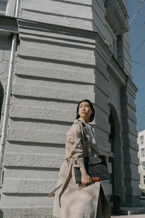 Woman in Beige Trench Coat Walking near a Concrete Building