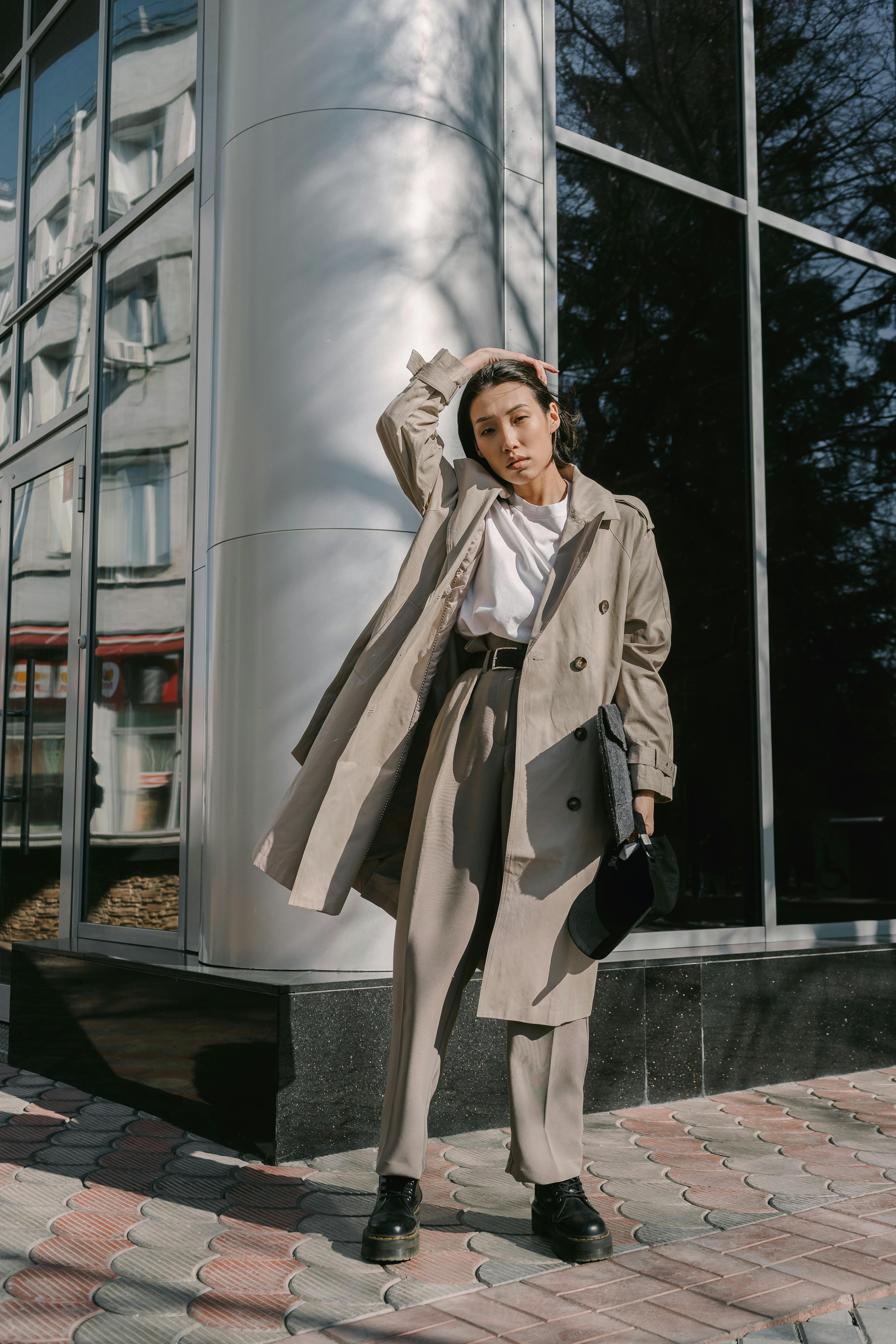 Fashionable woman posing in a chic outfit outdoors with modern architecture backdrop.