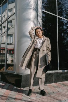 Fashionable woman posing in a chic outfit outdoors with modern architecture backdrop.