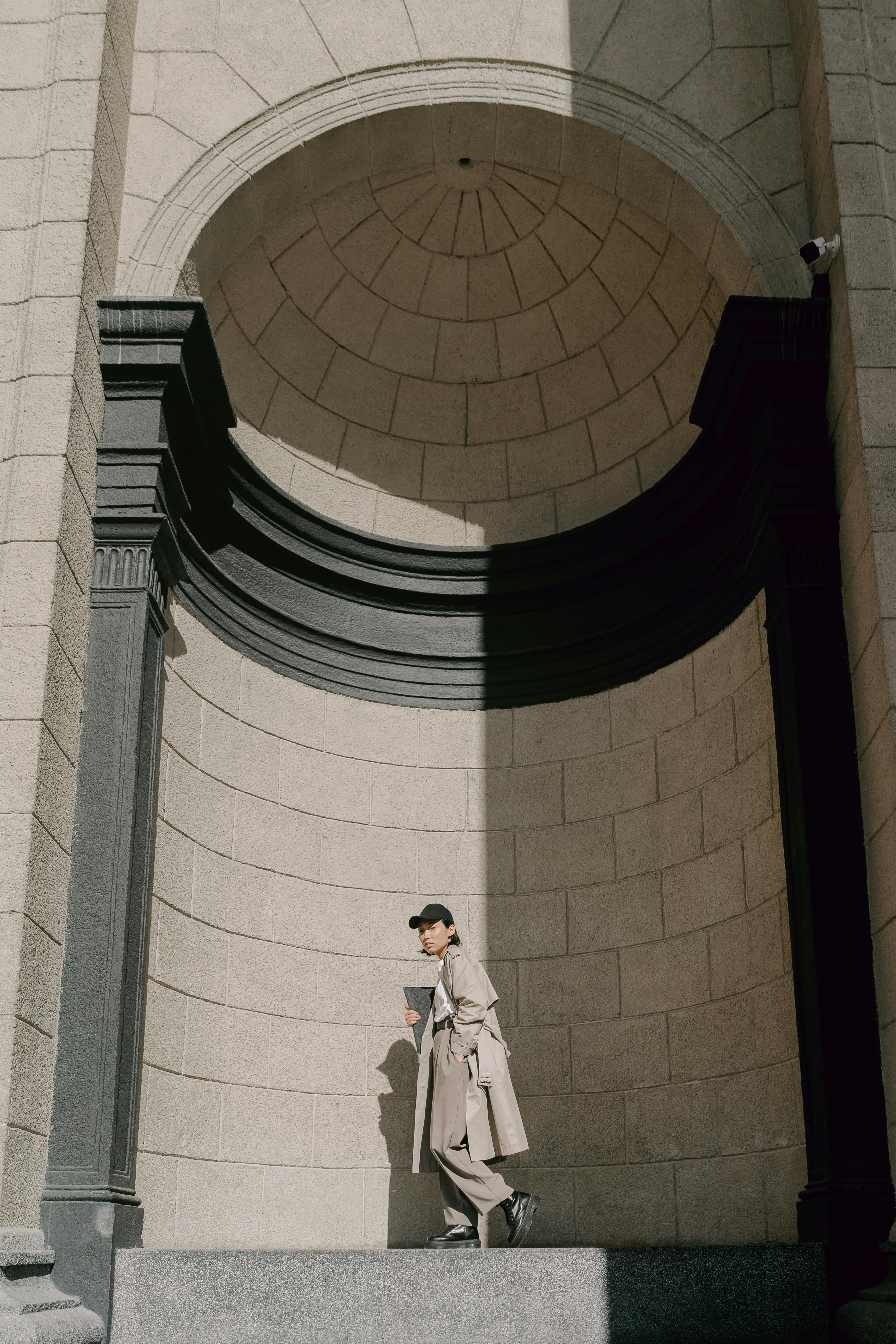 A stylish woman in a trench coat walks by a grand architectural structure, blending urban fashion with classic design.