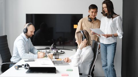 A diverse group of coworkers collaborating in a modern office space with headsets and laptops.