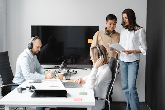 A diverse group of coworkers collaborating in a modern office space with headsets and laptops.