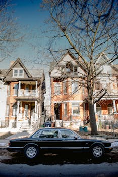 A sleek black luxury car parked along a historic residential street with old brick houses.