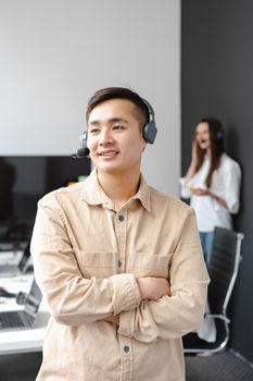 Smiling call center operator in a modern office with arms crossed, wearing a headset.