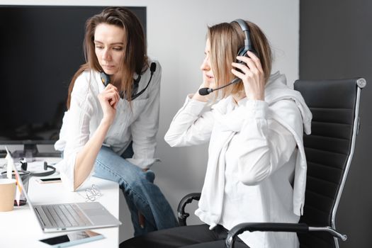 Two women working in a call center, wearing headsets and engaging in a team discussion.