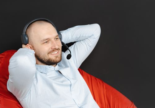 Smiling call center agent relaxed with hands behind head, wearing headset.