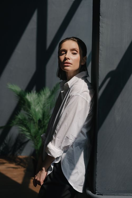 Free Artistic portrait of a woman leaning against a wall, bathed in dramatic sunlight and shadows. Stock Photo