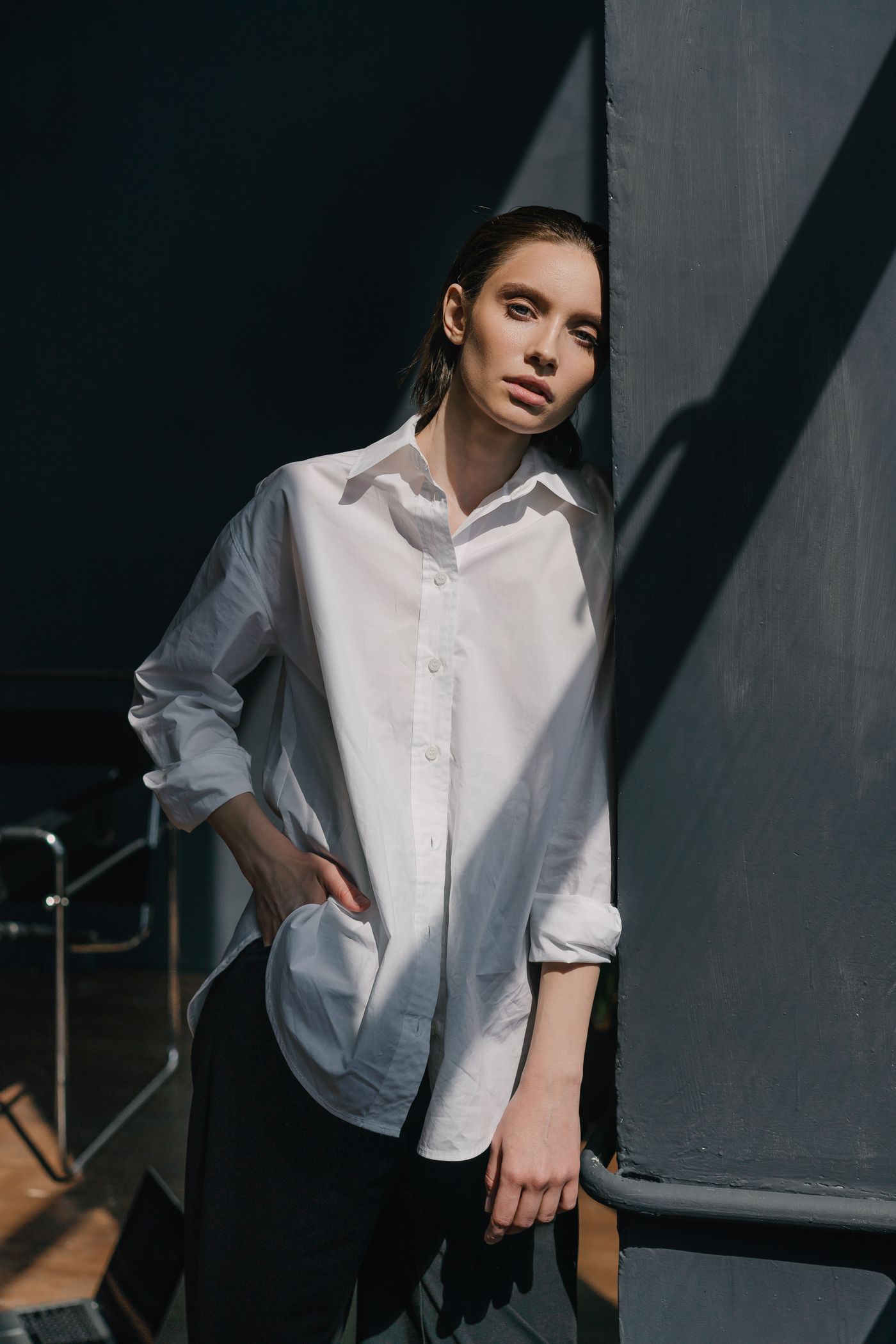 A woman in a dress shirt leaning on a black wall — the white shirt, the CBK signature