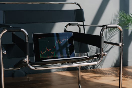 A sleek tablet on a designer chair shows a dynamic stock market chart under natural light.