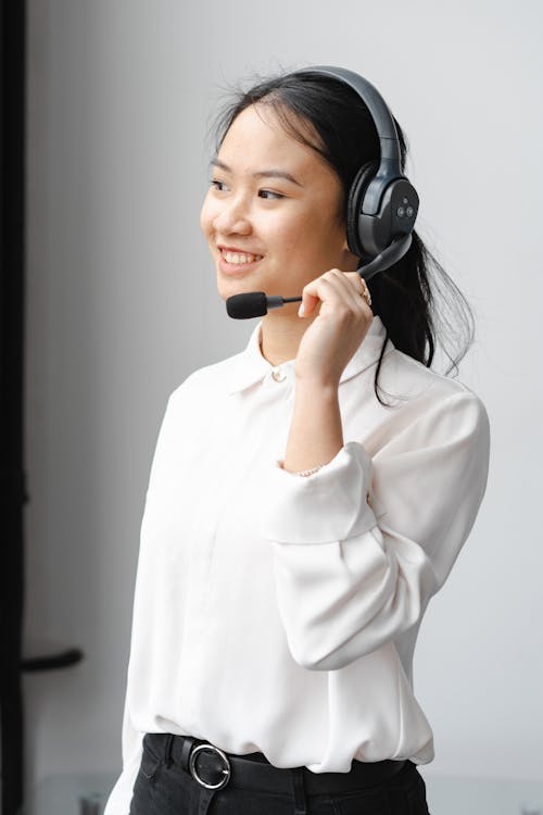 Photo of a Woman Smiling while Holding the Microphone of Her Headset