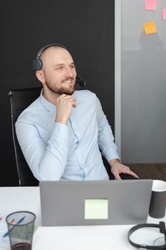 Smiling male customer service agent in an office wearing a headset and working on a laptop.