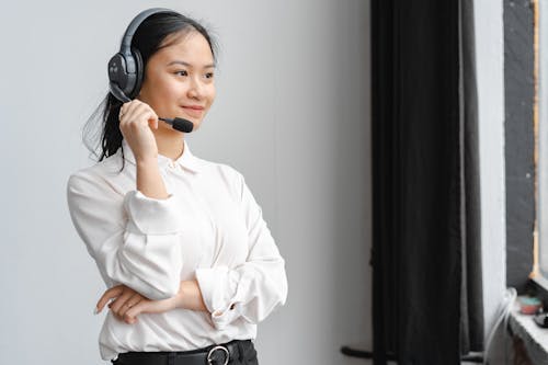 Free Woman in a White Long Sleeve Shirt Holding the Mic of Her Headset Stock Photo