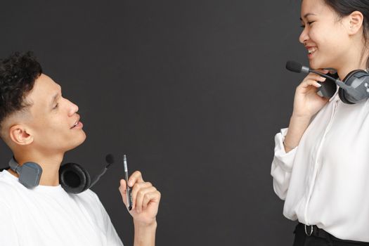 Two customer service agents with headsets engaged in a friendly conversation against a gray background.