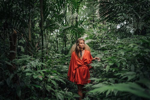 Photo of a Woman in a Red Silk Dress Touching Green Plants