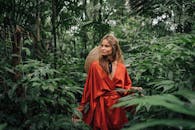 一个穿着红色长袍的时尚女人在郁郁葱葱的丛林绿地中摆姿势，创造了一个充满活力和异国情调的场景