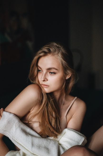 Young dreamy woman in bra and sweater sitting in dark place while looking away