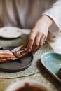 Crop anonymous female with knife cutting sweet pastry on plate on table in light place