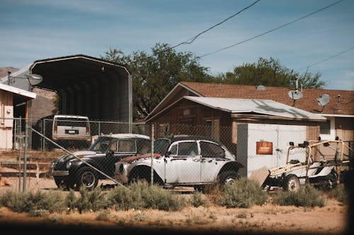 Retro vehicles parked near metal grid and building under blue sky in backyard in daylight