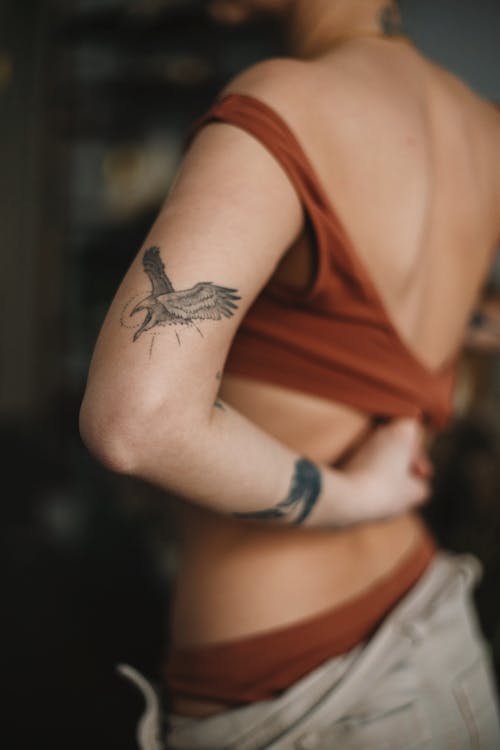 Crop tattooed woman putting on tank top