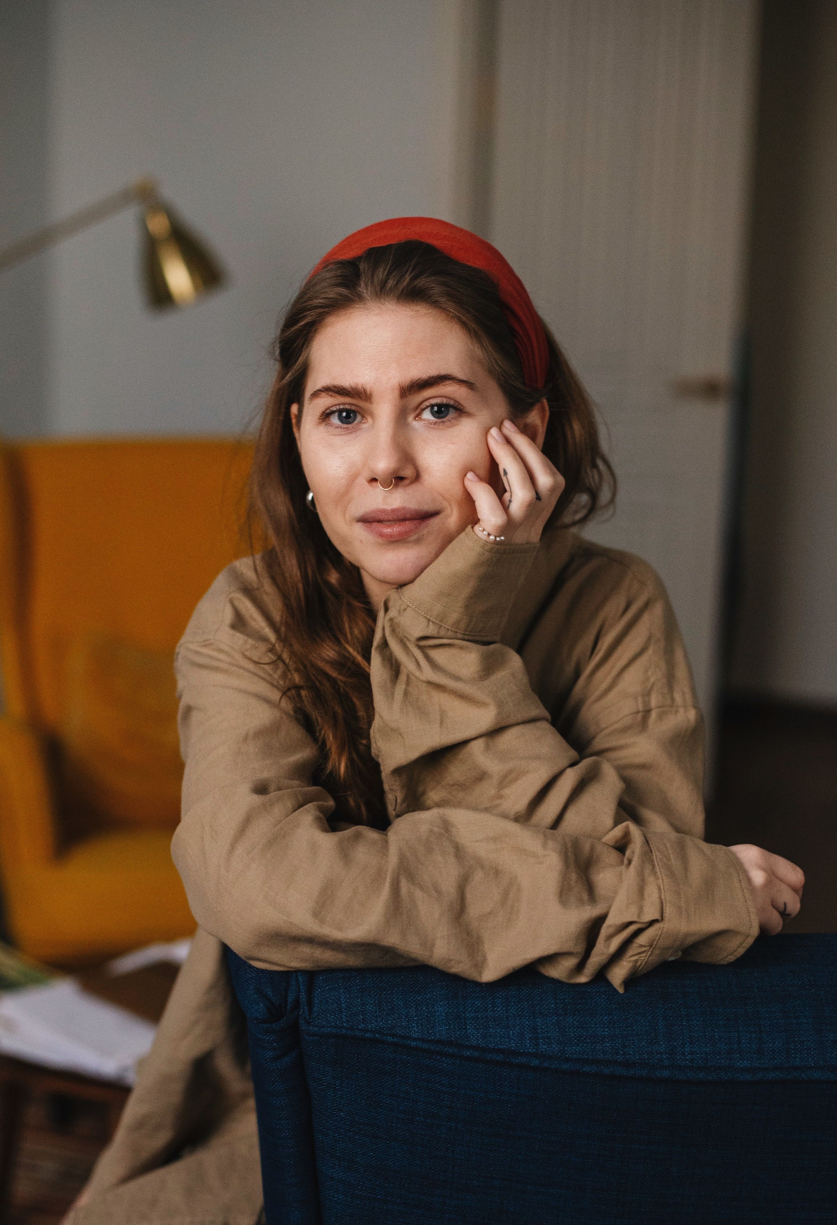 Content female looking at camera and leaning on hand while sitting on sofa in room against blurred background