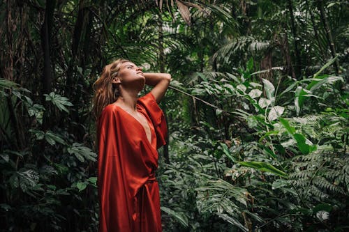 A Woman in Red Dress Standing Near Green Plants