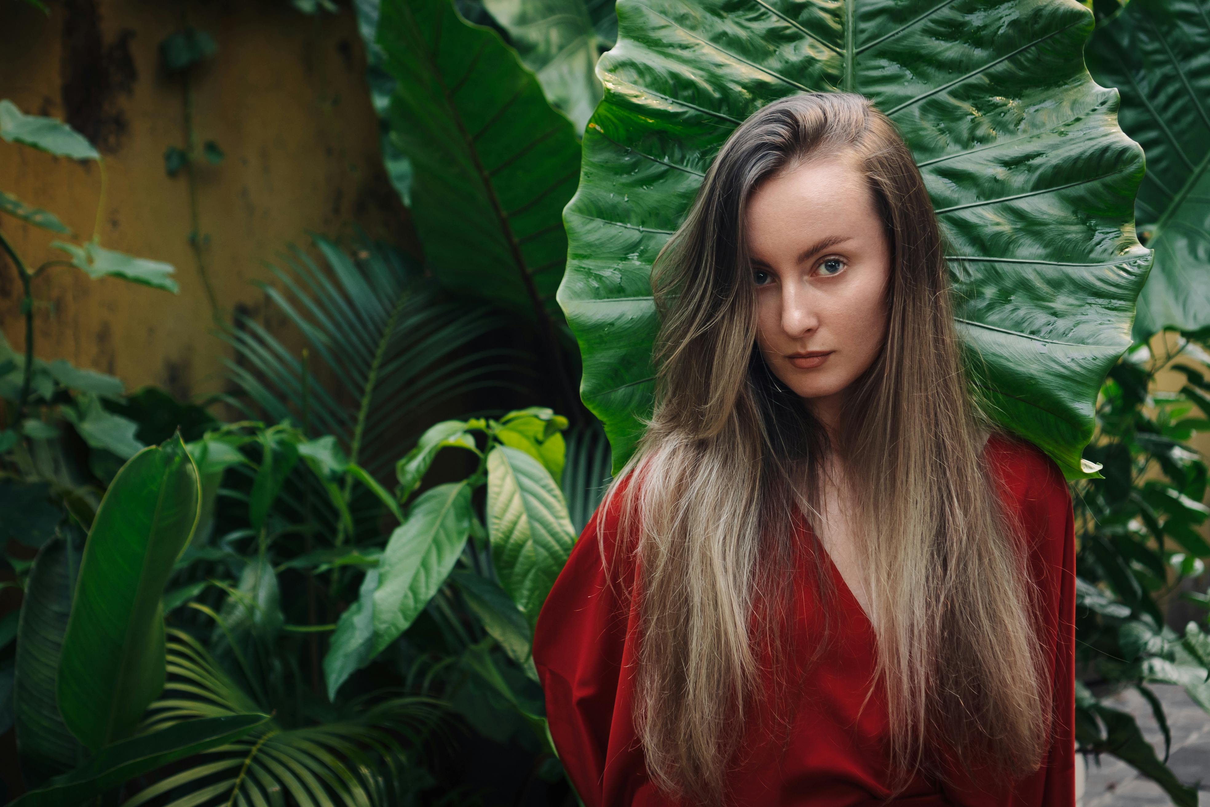 woman in red shirt standing beside green leaves