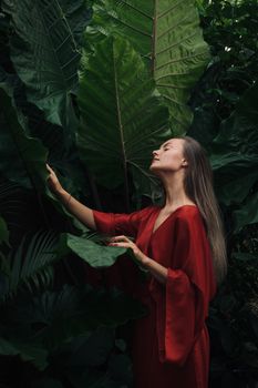 Woman in Red Dress Standing Beside Green Leaves