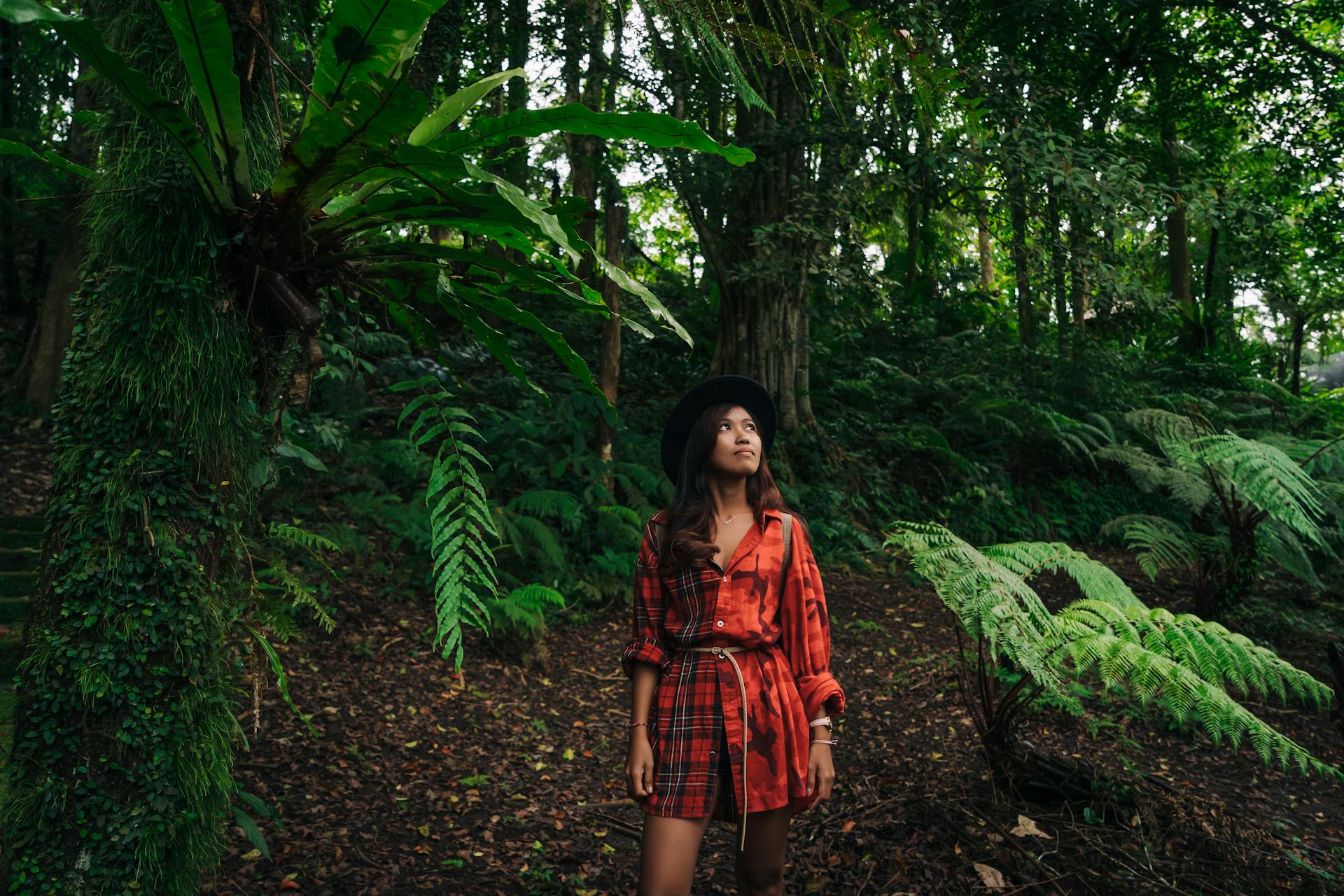 A woman in a red dress exploring a vibrant green forest filled with ferns and trees.