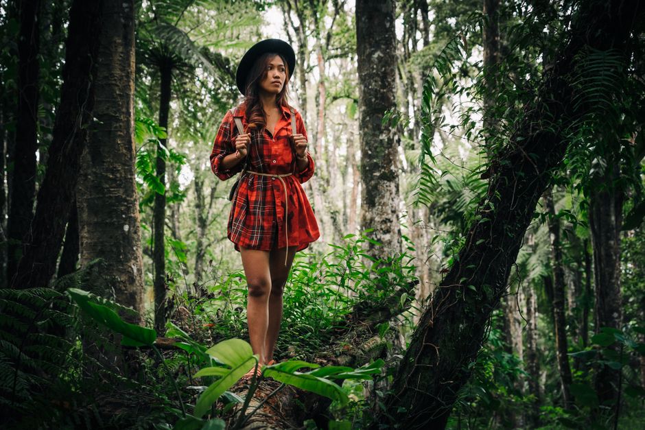 A woman in a plaid shirt hikes through a lush green forest, embodying adventure and exploration.
