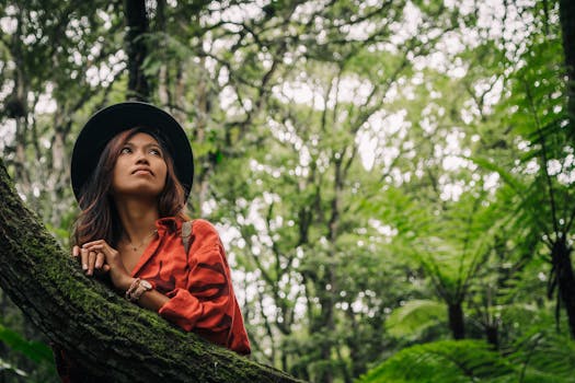 Asian woman in red shirt and hat admiring nature in a green forest setting.
