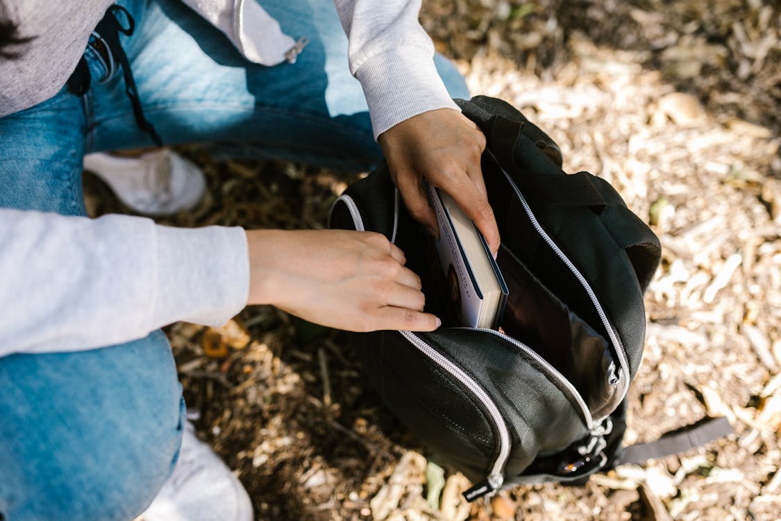 Person Putting a Booking Inside a Backpack · Free Stock Photo