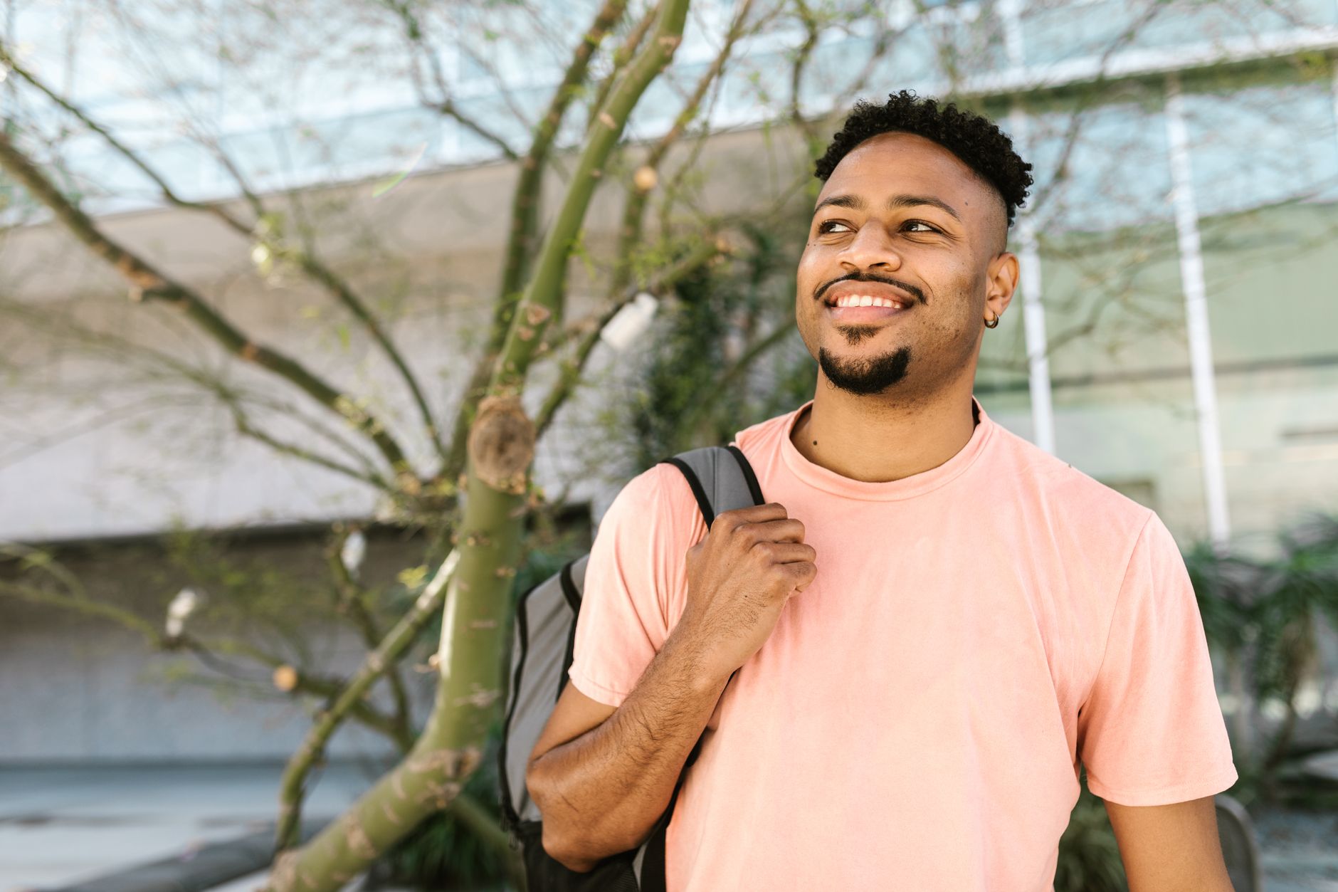 Cheerful young man outdoors with a backpack, embracing a sunny day.