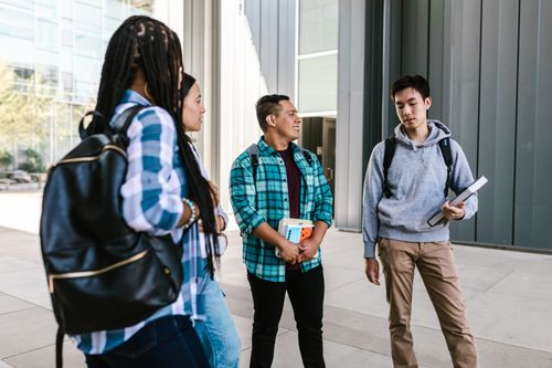 Free A group of university students socializing and holding books outside on campus. Stock Photo