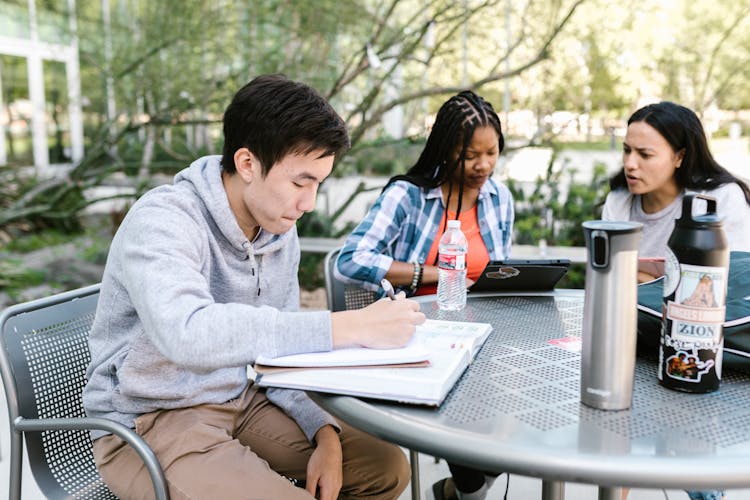 Students Sitting At The Table In The Park Writing In The Notebook