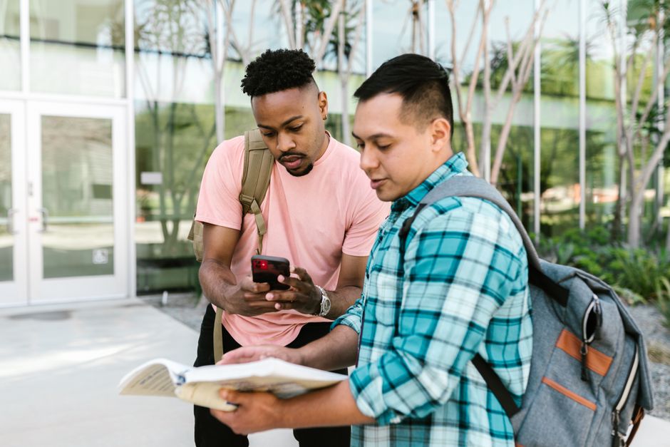 Two students reviewing notes on campus, collaborating for an exam outside. Two students reviewing notes on campus, collaborating for an exam outside.