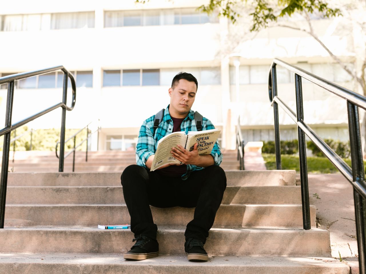 An Asian male student reading a book on the campus steps