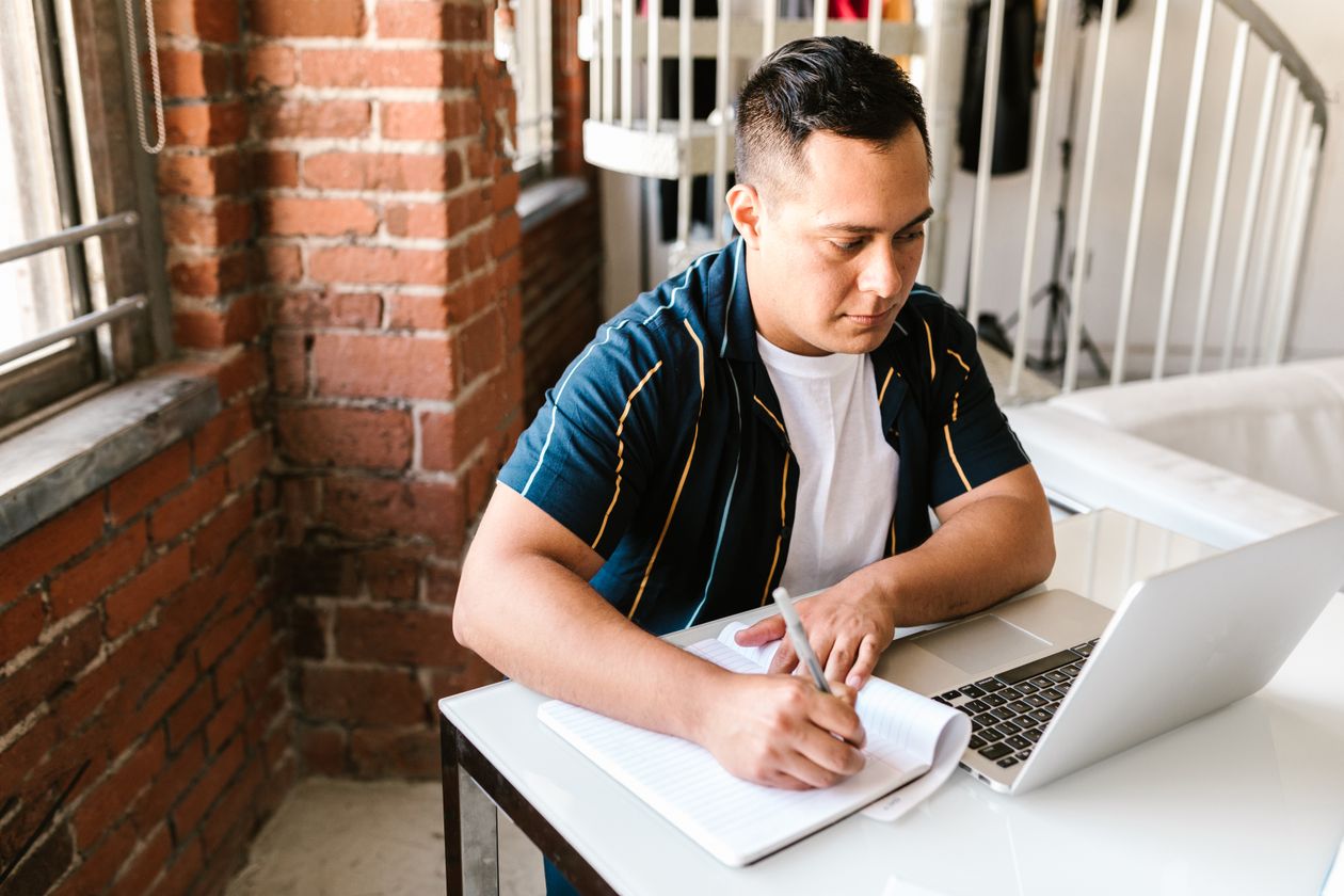 Young man studying with a laptop and notebook, weighing the Side Hustle Summit against traditional online courses