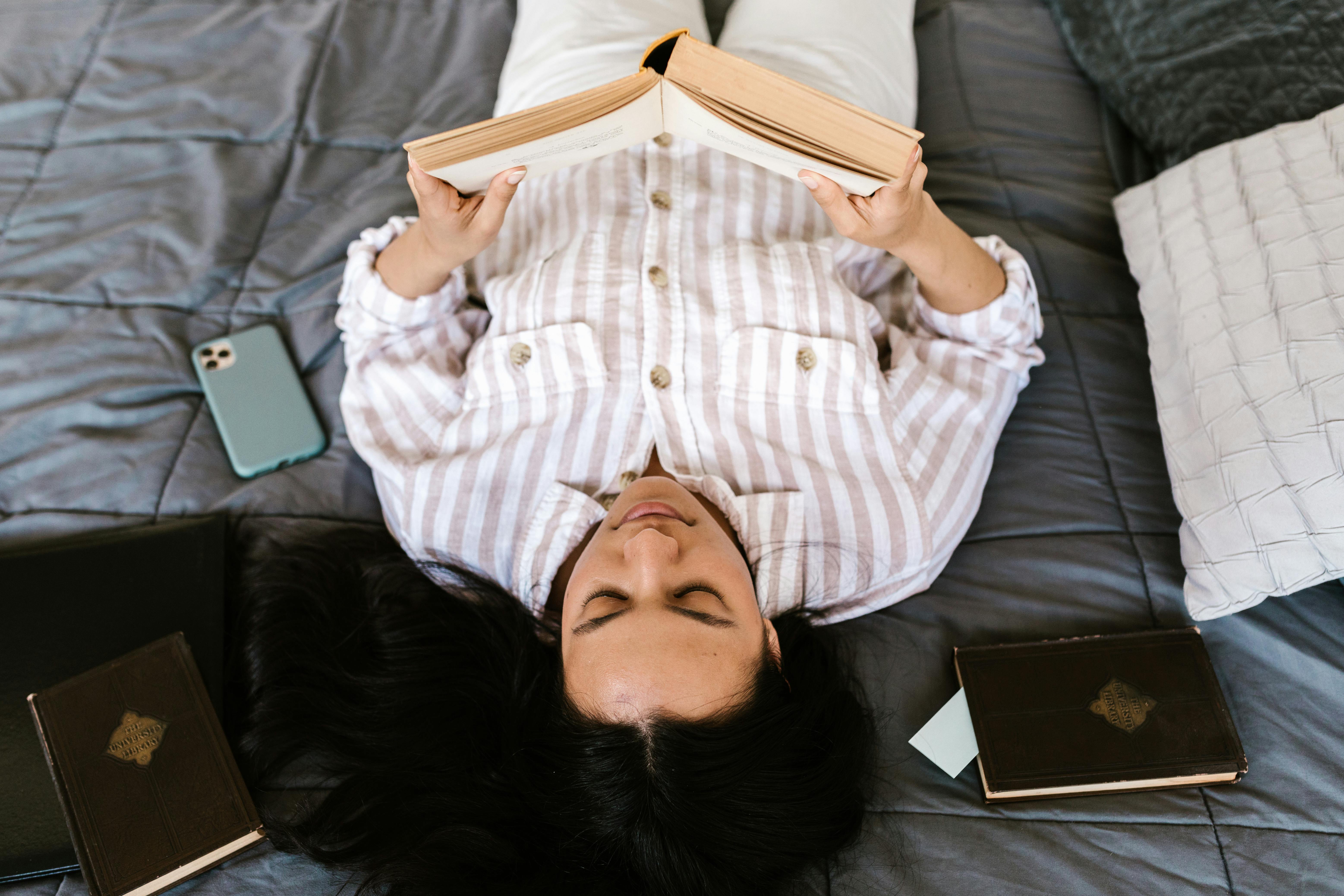 a young woman reading a book while lying down on a bed