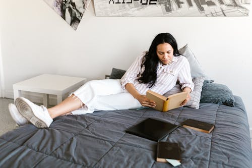 A Woman Reading a Book while Sitting on a Bed