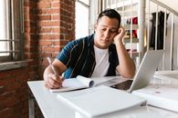 A Bored Man Writing on a Notebook