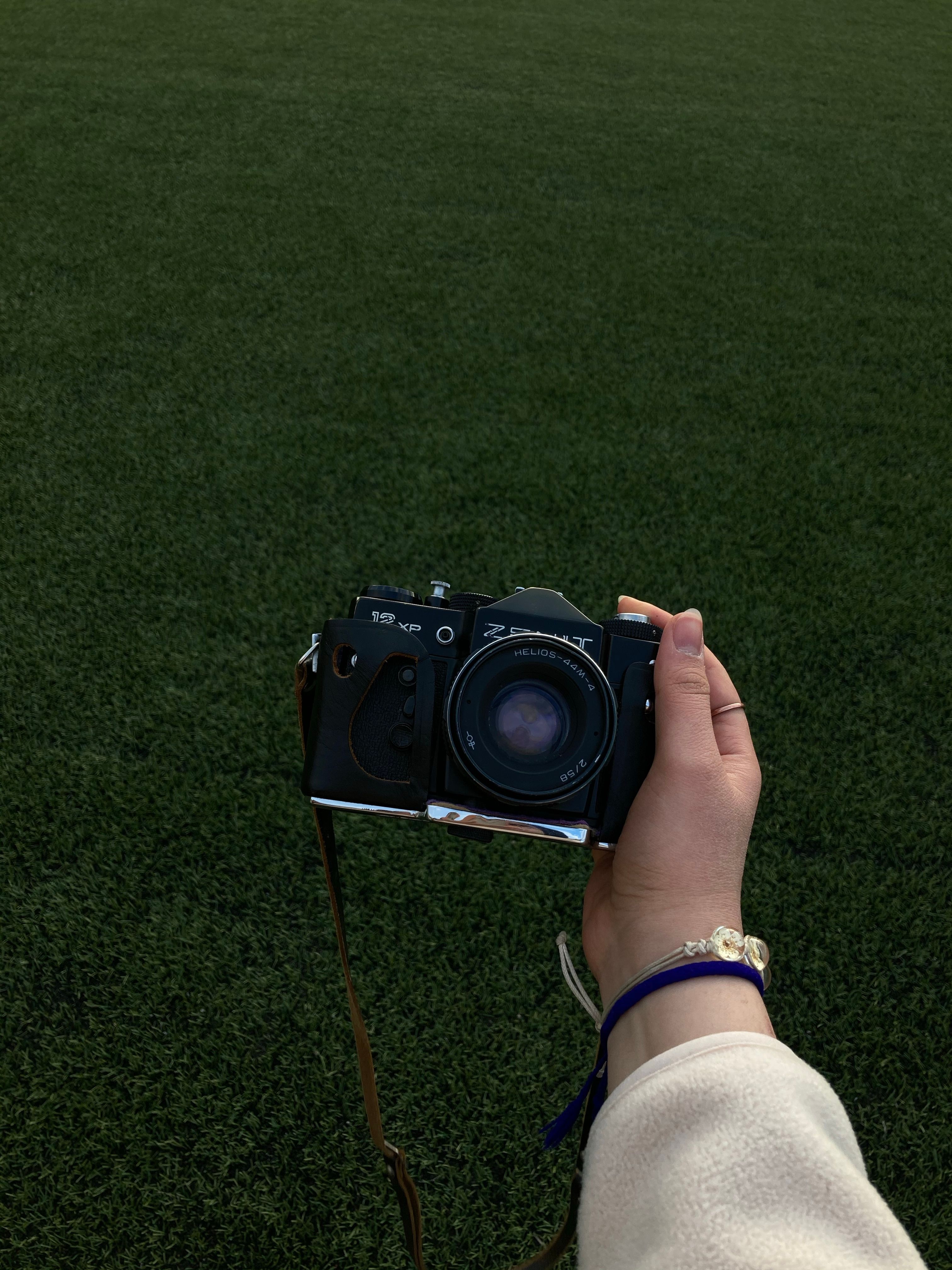 A close-up of a hand holding a vintage camera with a green field backdrop, showcasing retro style.