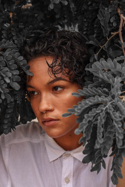 Free A woman with curly hair and piercing poses amidst dark leaves, conveying introspection. Stock Photo